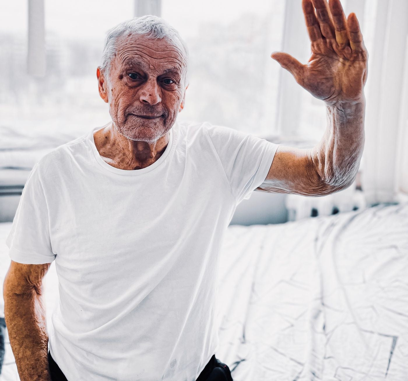 Smiling older man with white hair waving in a bright room